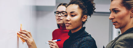 Three Women Discussing Something on a White Board